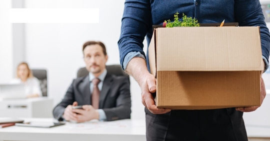 Man carrying out belonging in cardboard box while other man and woman watches him leave